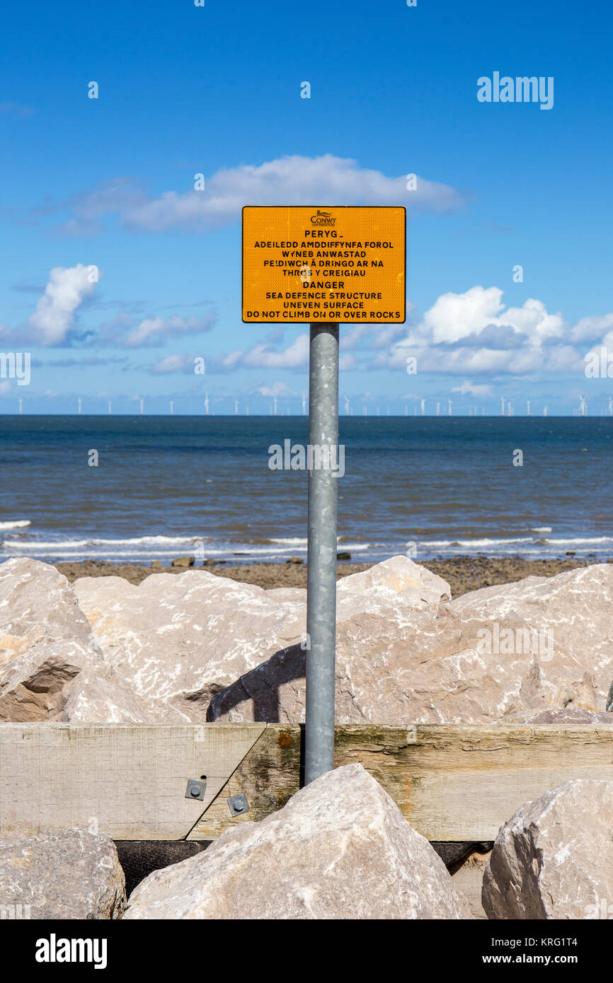 Danger warning sign Sea defence structure uneven surface. Do not climb on or over rocks near Llanddulas North Wales UK Stock Photo