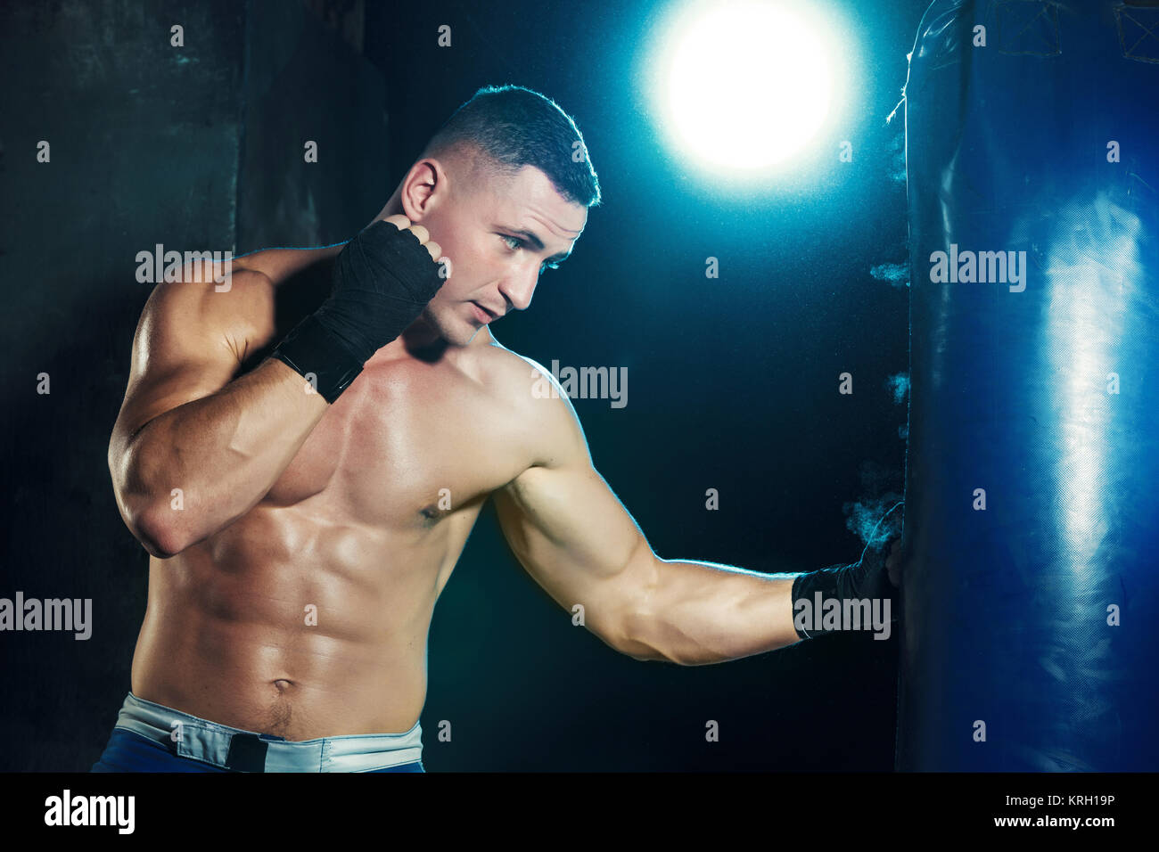 Male boxer boxing in punching bag with dramatic edgy lighting in a dark ...