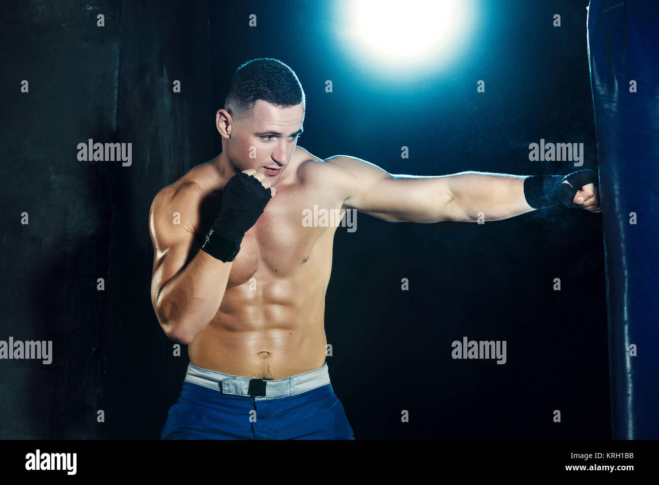 Male boxer boxing in punching bag with dramatic edgy lighting in a dark ...