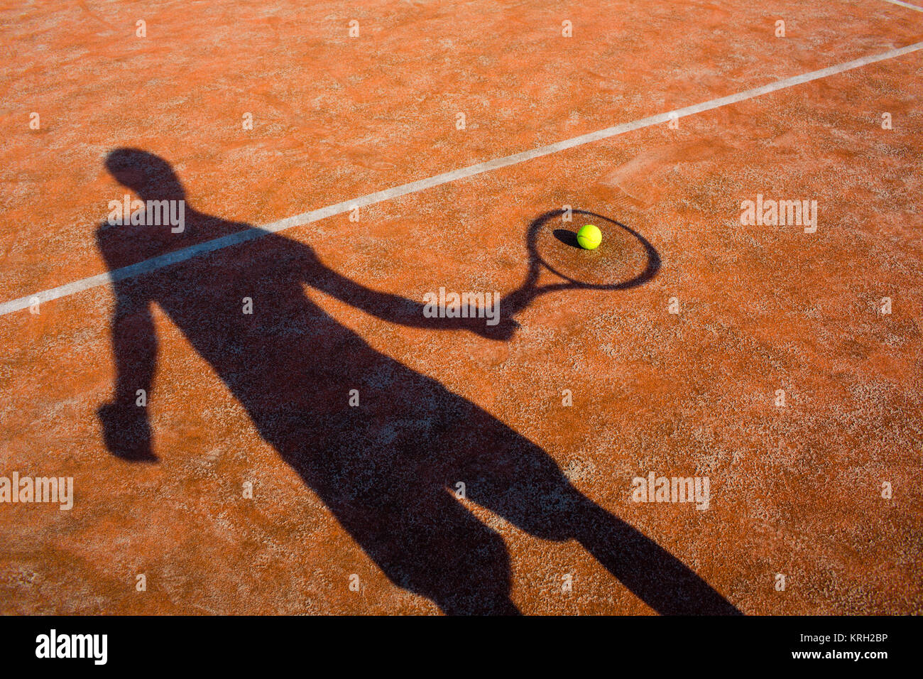 shadow of a tennis player in action on a tennis court (conceptual image with a tennis ball lying on the court and the shadow of the player positioned in a way he seems to be playing it) Stock Photo