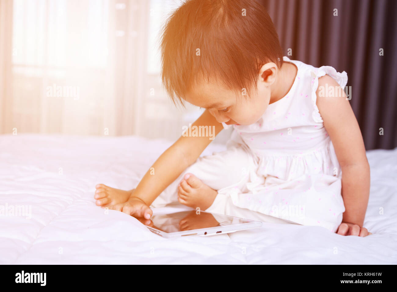 baby are looking to play and read tablet computer on bed at home Stock Photo