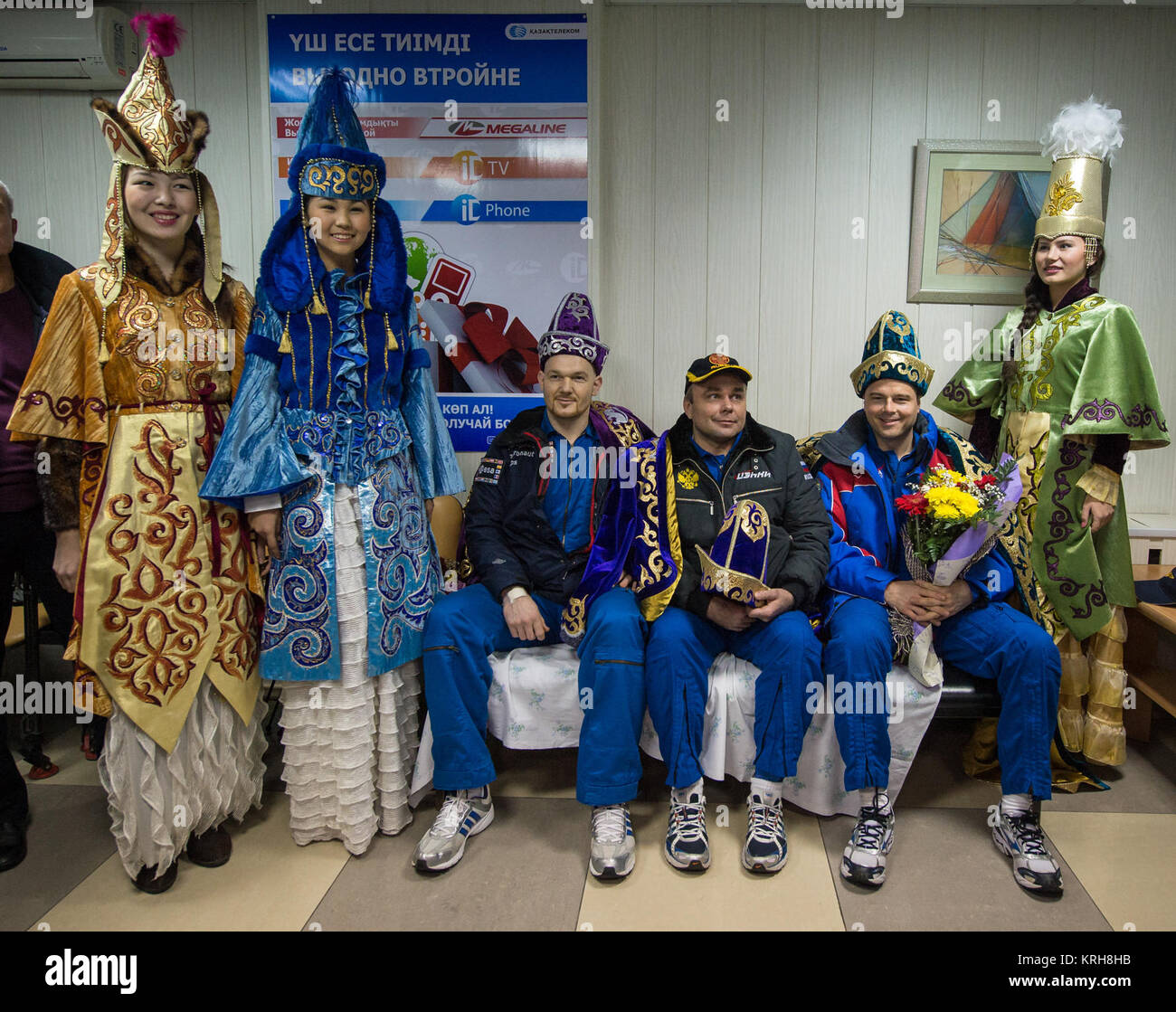 Expedition 41 light Engineer Alexander Gerst of the European Space Agency (ESA), seated left, Commander Max Suraev of the Russian Federal Space Agency (Roscosmos), center, and NASA Flight Engineer Reid Wiseman, pose for a photograph with women in kazakh ceremonial dress during a welcome ceremony at the Kustanay Airport shortly after they arrived there via helicopter from their Soyuz landing site in a remote area near the town of Arkalyk, Kazakhstan on Monday, Nov. 10, 2014. Suraev, Wiseman and Gerst returned to Earth after more than five months onboard the International Space Station where the Stock Photo