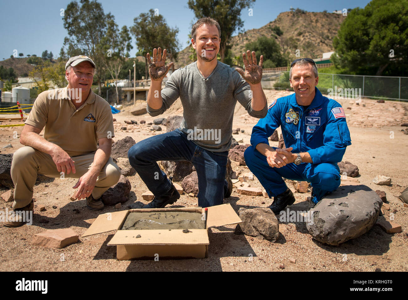 Actor Matt Damon, who stars as NASA Astronaut Mark Watney in the film “The Martian,” smiles after having made his hand prints in cement at the Jet Propulsion Laboratory (JPL) Mars Yard, while Mars Science Lab Project Manager Jim Erickson, left, and NASA Astronaut Drew Feustel look on, Tuesday, Aug. 18, 2015, at the JPL in Pasadena, California. While at JPL Damon meet with NASA scientists and engineers who served as technical consultants on the film. The movie portrays a realistic view of the climate and topography of Mars, based on NASA data, and some of the challenges NASA faces as we prepare Stock Photo
