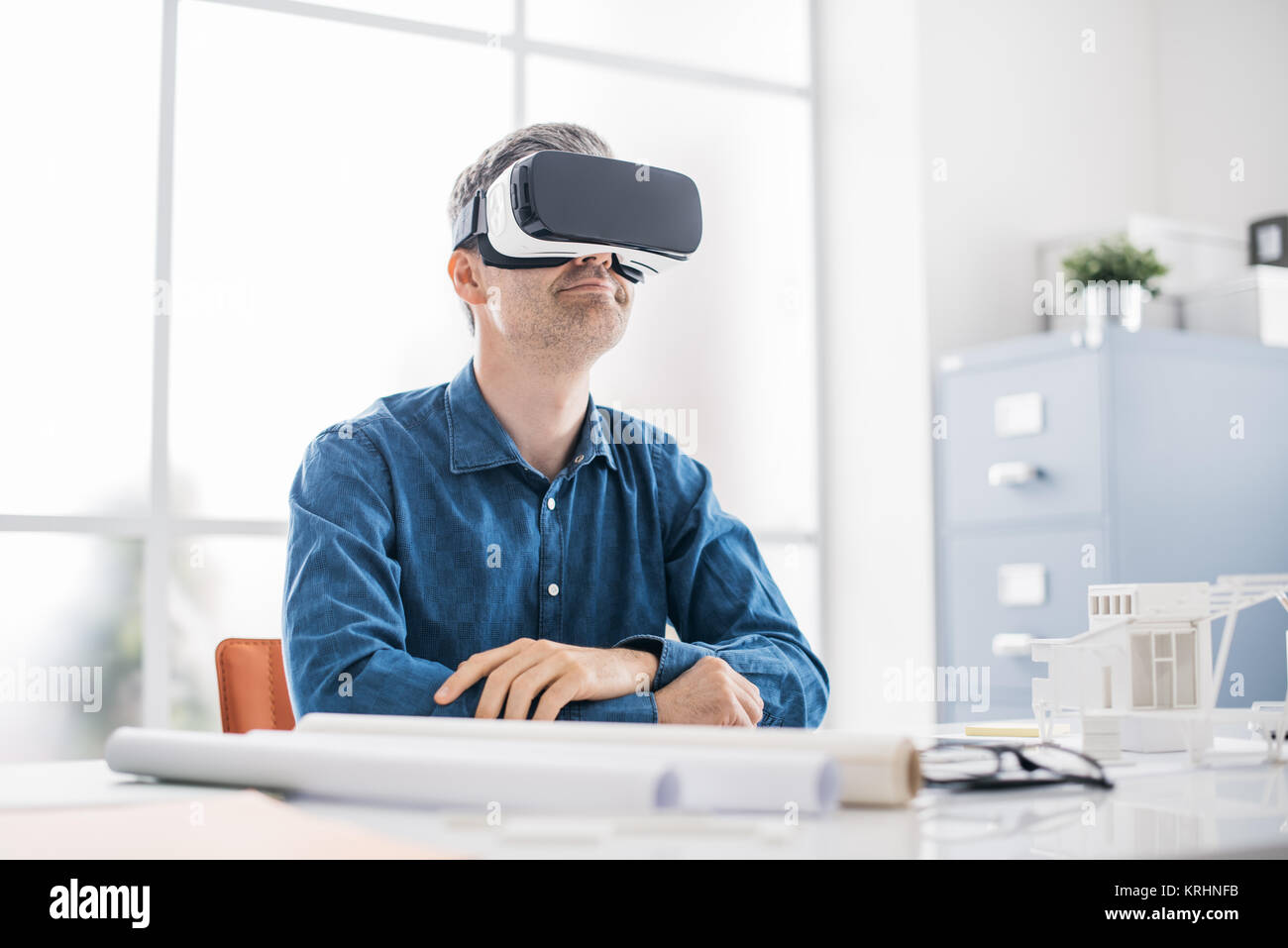 Professional architect working at office desk and wearing a VR headset, he is viewing a virtual reality interface Stock Photo