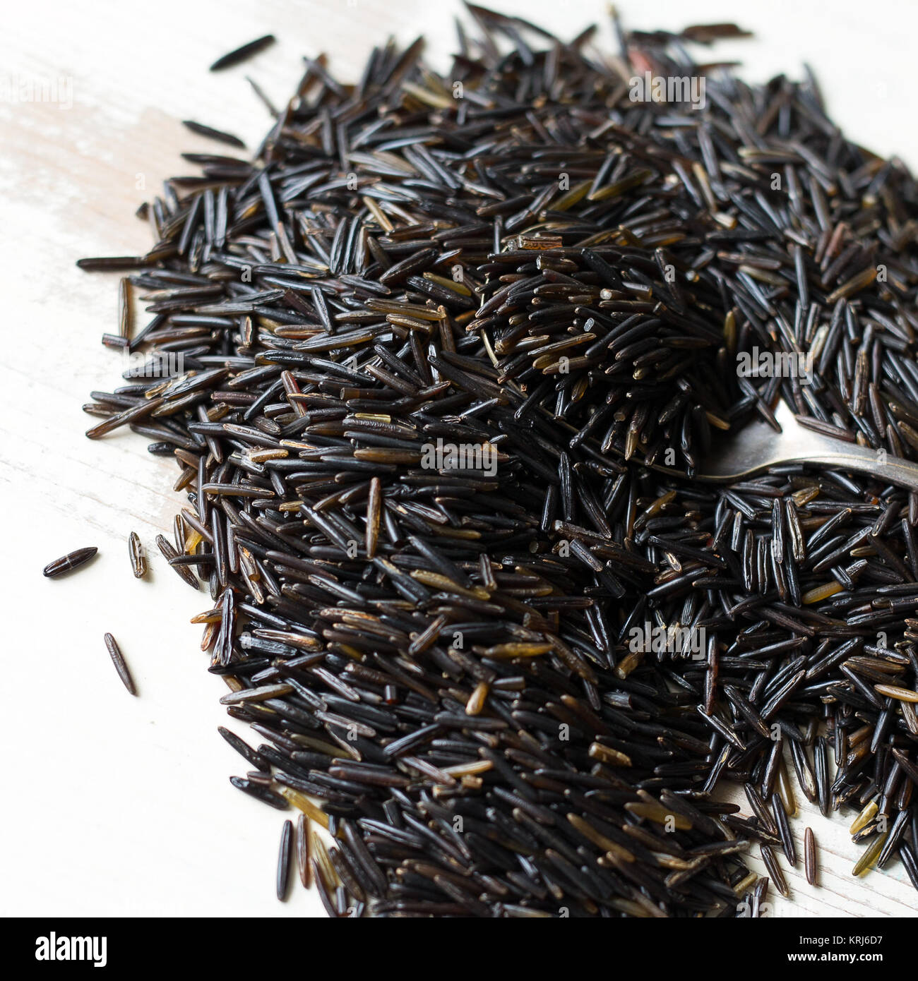 Wild rice in a small pile on a wooden background. Shown with silver spoon. Stock Photo