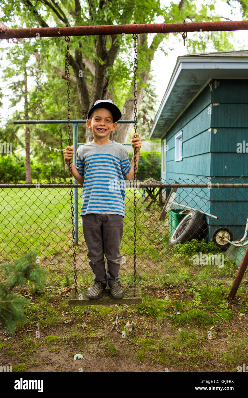 Smiling mixed race boy standing on backyard swing Stock Photo