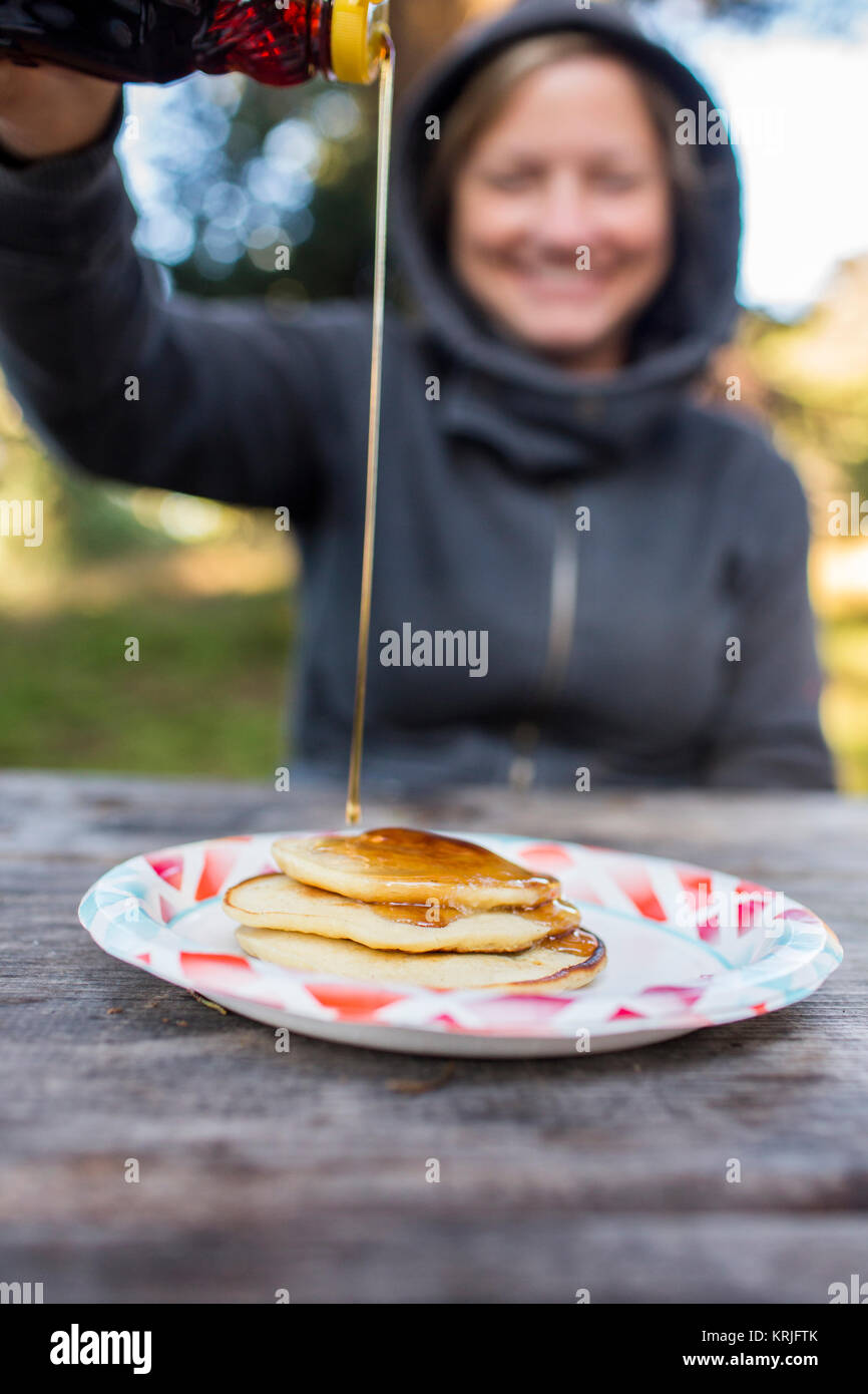 Smiling Caucasian woman pouring syrup on pancakes Stock Photo
