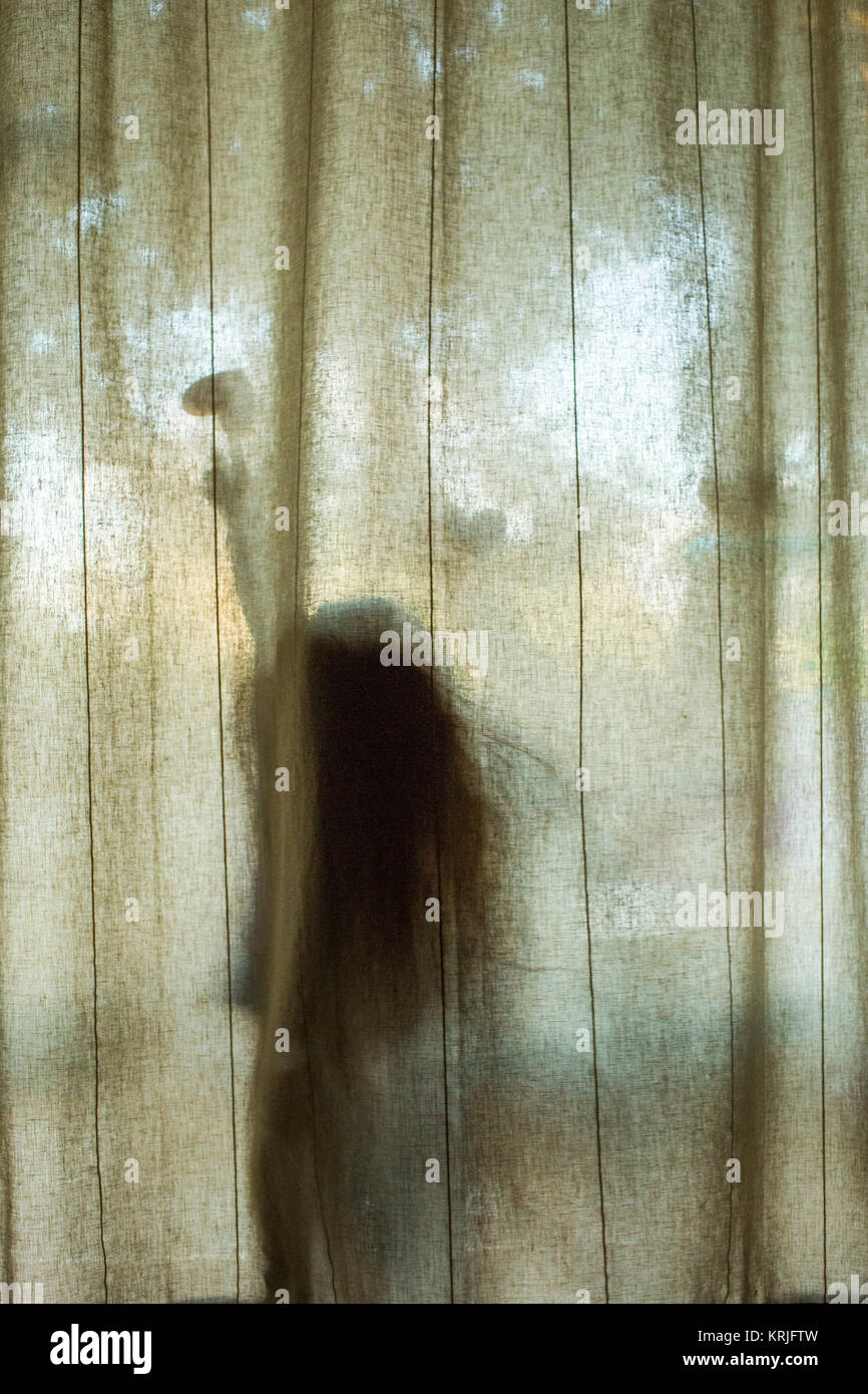 Silhouette of Caucasian girl touching heart-shape behind window curtain Stock Photo