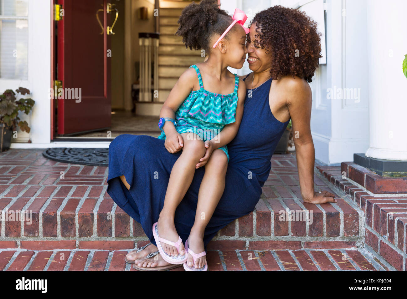 Smiling mixed race mother and daughter rubbing noses on front stoop Stock Photo