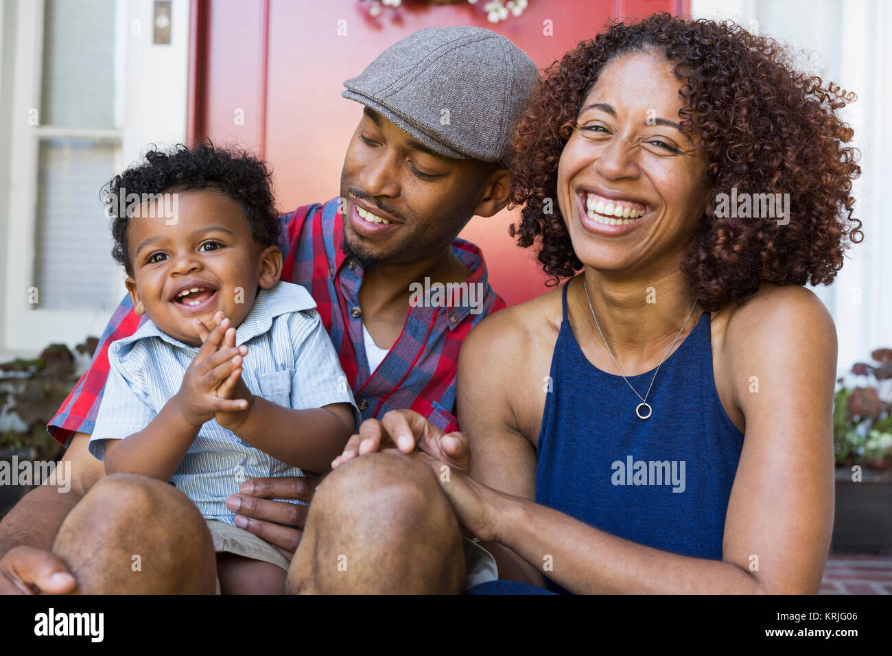 Laughing mixed race couple sitting on front stoop with son Stock Photo