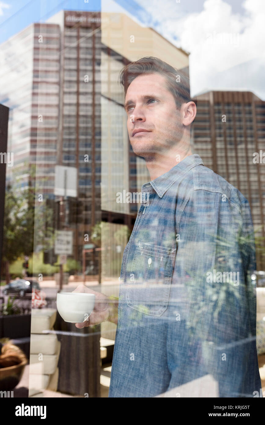 Pensive Caucasian man drinking coffee near window in city Stock Photo