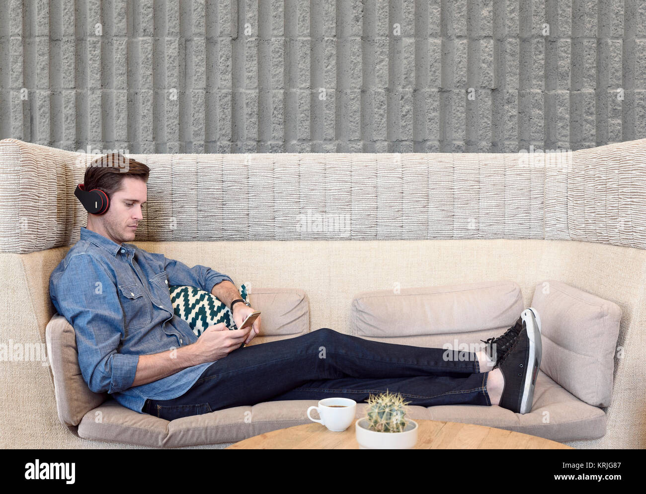 Caucasian man sitting on sofa wearing headphones texting on cell phone Stock Photo