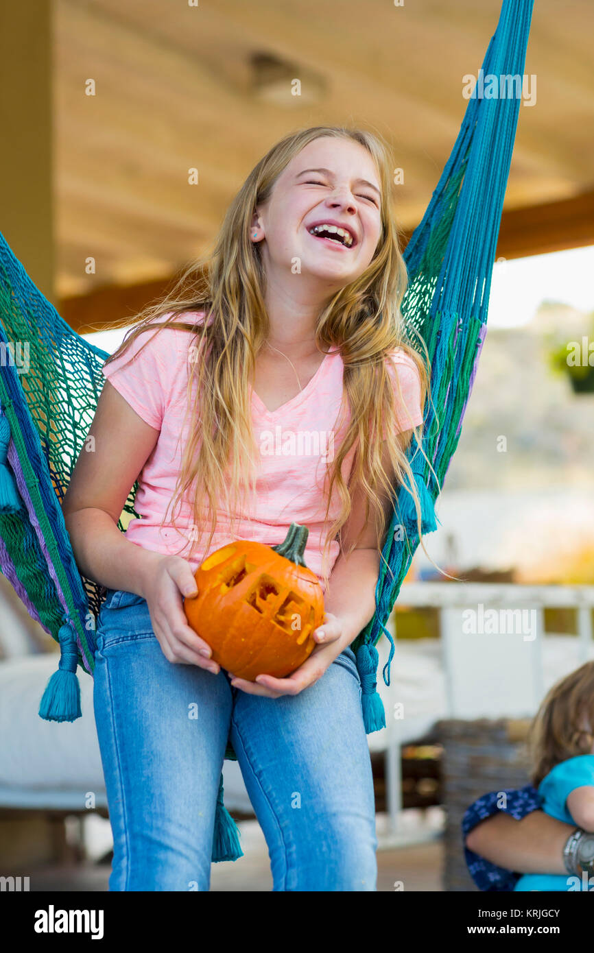 Laughing Caucasian girl in hammock holding pumpkin Stock Photo