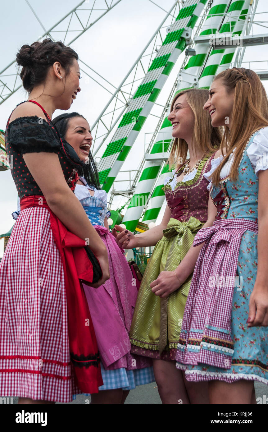 Attractive and joyful woman at German Oktoberfest with traditional dirndl dresses, big wheel in the background. Stock Photo