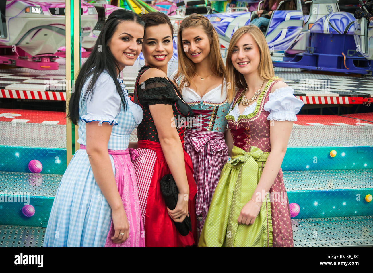 Attractive and joyful woamn at German Oktoberfest with traditional dirndl dresses and joyride in the background. Stock Photo