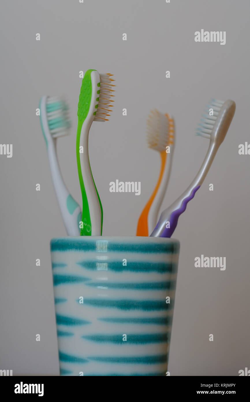 Vier verschiedenfarbige Zahnbürsten in Keramikbecher  einander zugewandt Stock Photo