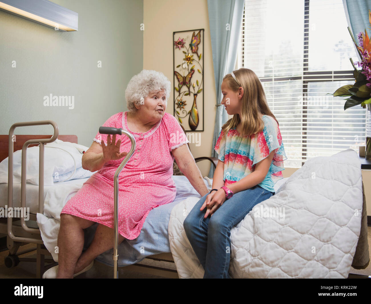 Smiling Caucasian woman sitting on bed talking to granddaughter Stock Photo