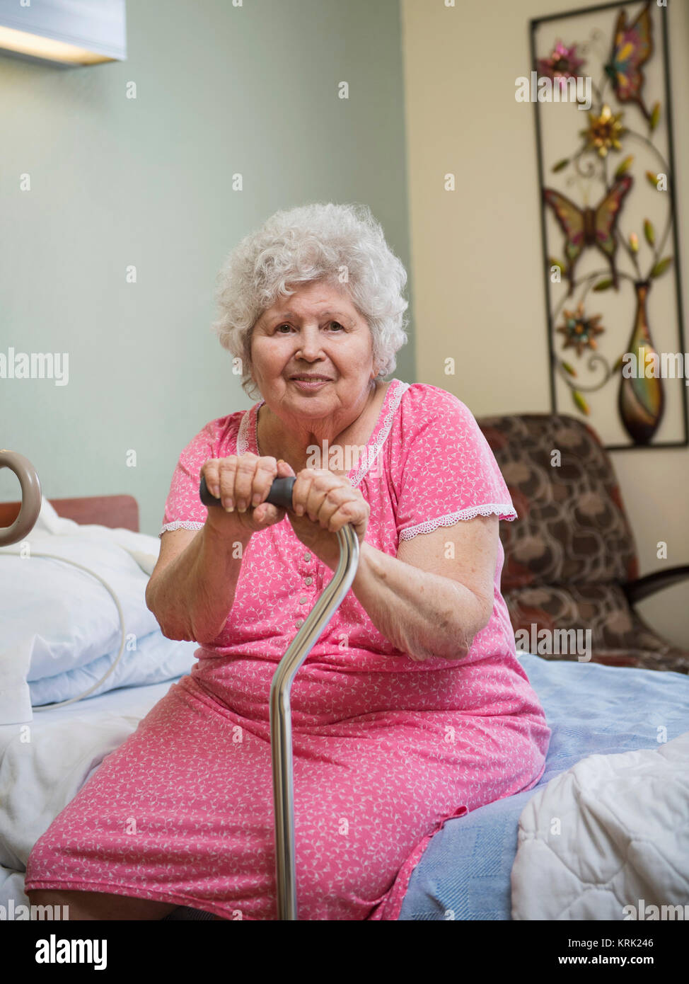 Smiling Caucasian woman sitting on bed leaning on cane Stock Photo