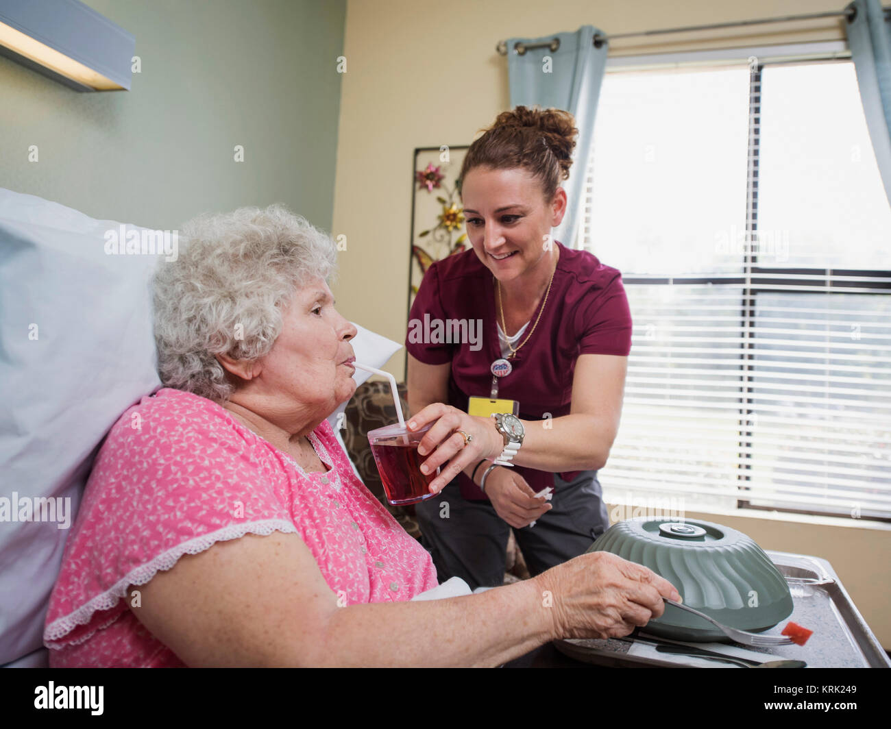 Caucasian nurse feeding patient in hospital bed Stock Photo