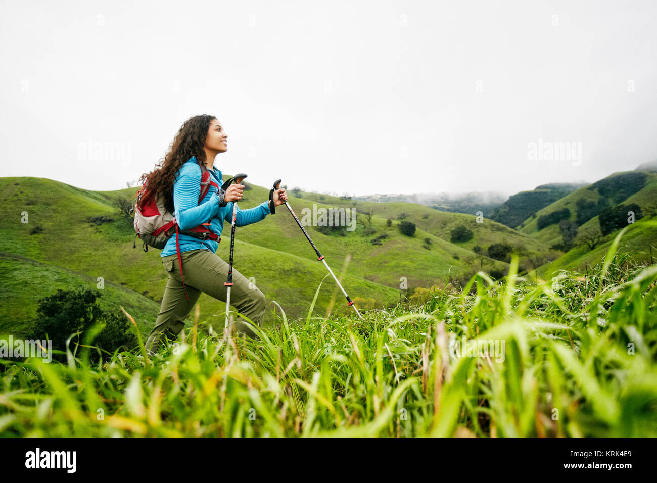 Smiling mixed race woman hiking with walking sticks Stock Photo