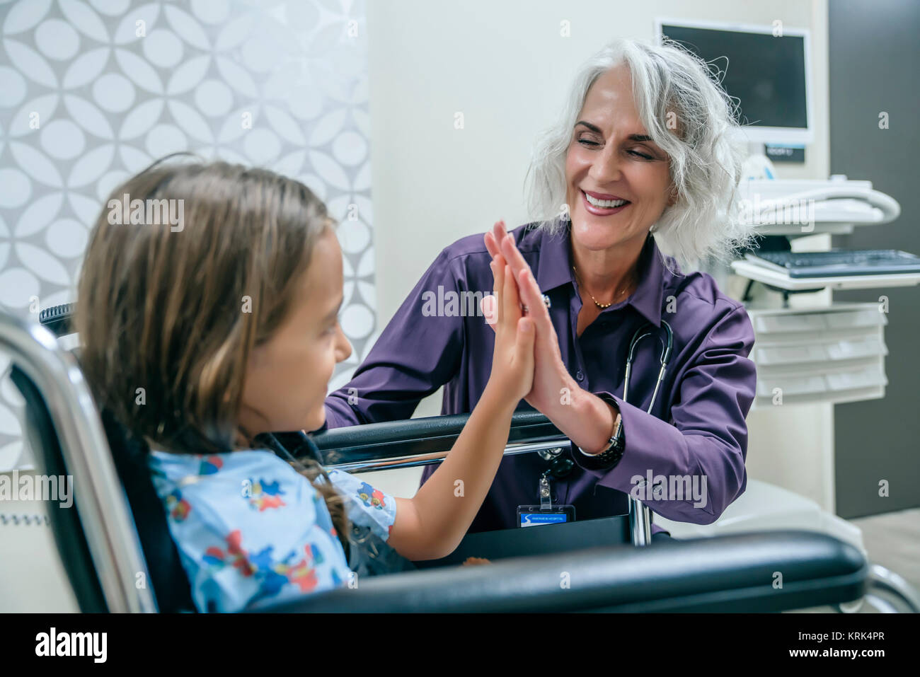 Doctor high-fiving girl in wheelchair Stock Photo