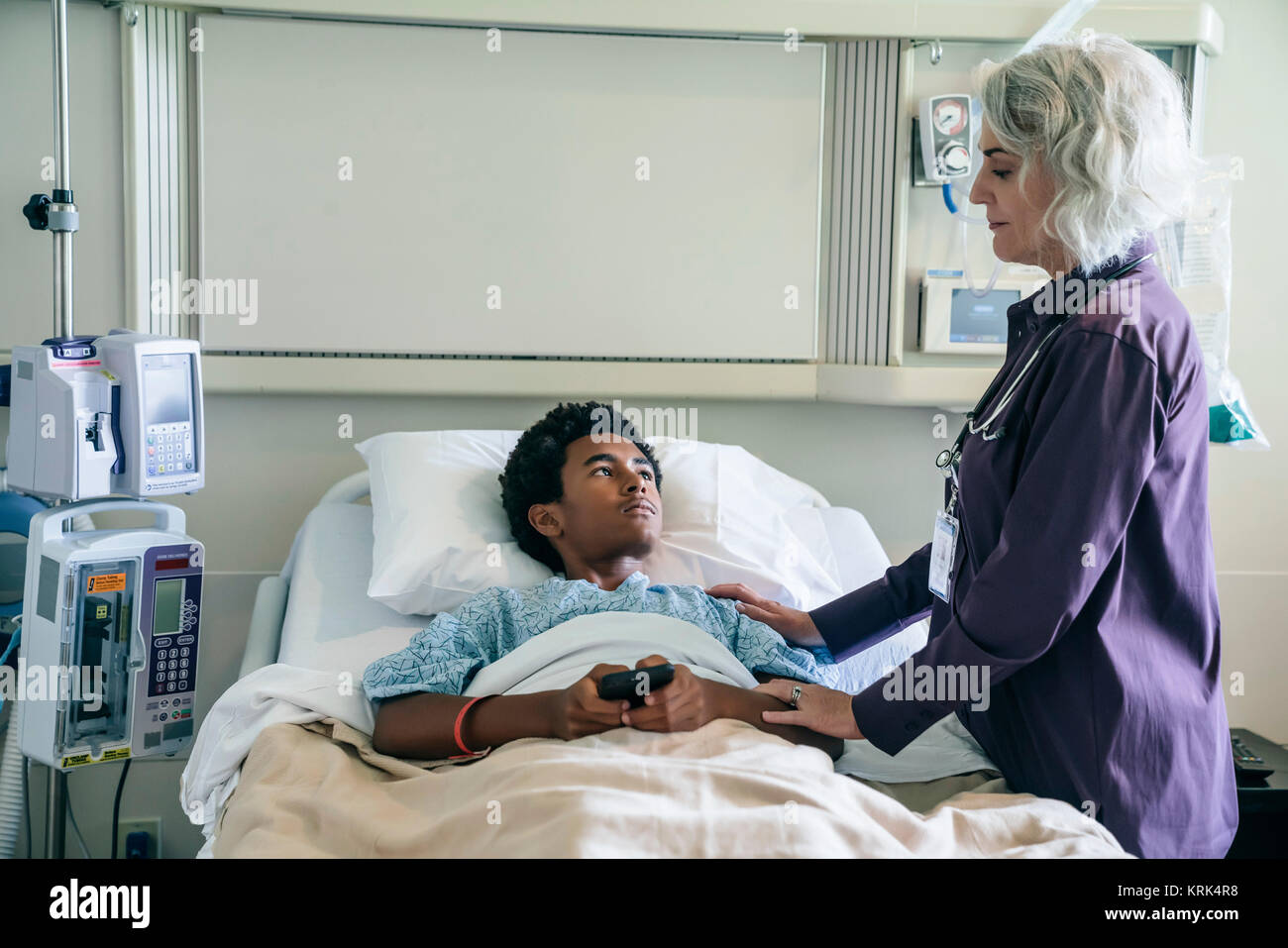 Doctor comforting boy in hospital bed holding cell phone Stock Photo