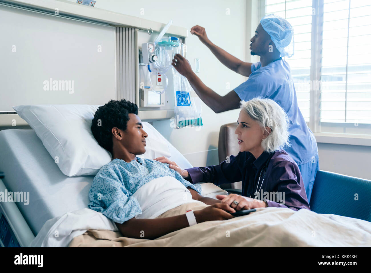 Doctor comforting boy laying in hospital bed Stock Photo