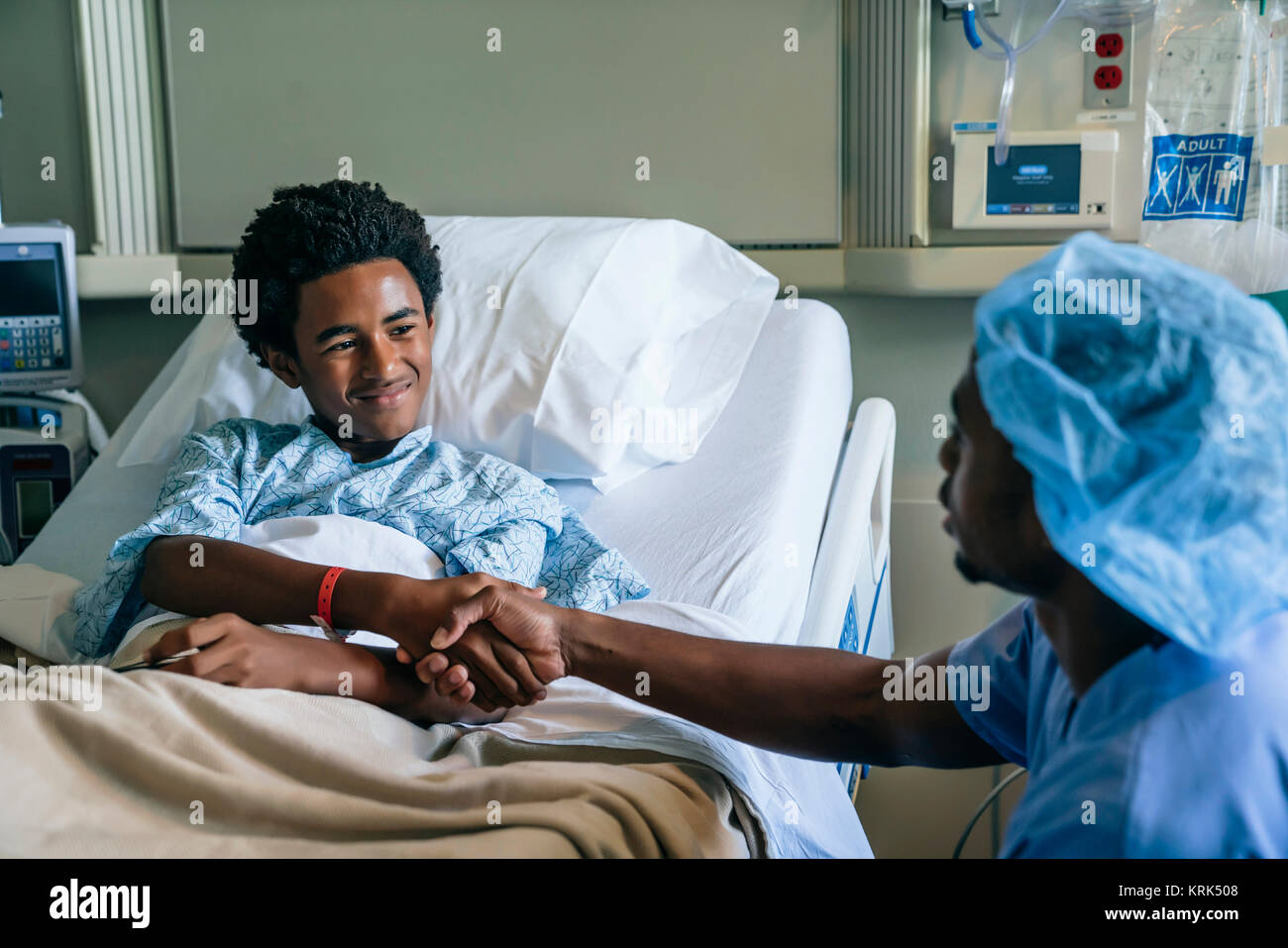 Black nurse shaking hands with boy in hospital bed Stock Photo