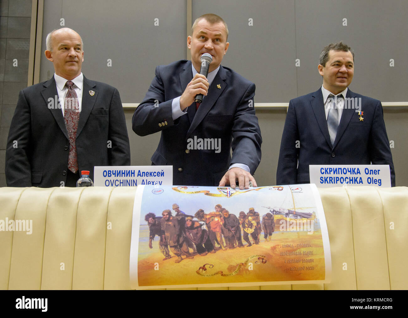 Expedition 47 Russian cosmonaut Alexei Ovchinin of Roscosmos, center, describes a poster created for him and his fellow crew members, NASA astronaut Jeff Williams, left, and Russian cosmonaut Oleg Skripochka during a crew press conference at the Gagarin Cosmonaut Training Center (GCTC), Friday, Feb. 26, 2016, in Star City, Russia.  The poster, a lighthearted take on the famous Russian painting 'Burlaki na Volge' by Ilya Repin, depicts Ovchinin, Skripochka, and Williams as part of a crew of Burlaks, or barge haulers, dragging a barge on the Volga river. Ovchinin has chosen Burlak as the Soyuz T Stock Photo