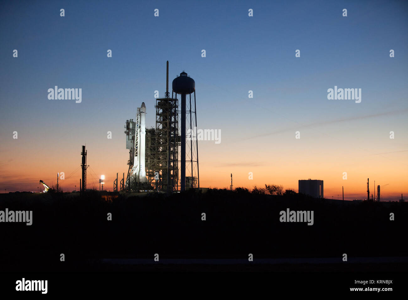 As sun sets, a Falcon 9 rocket stands ready for liftoff at the Kennedy Space Center's Launch Complex 39A. The historic launch site now is operated by SpaceX under a property agreement signed with NASA. In the background is the Vehicle Assembly Building. The rocket will boost a Dragon resupply spacecraft to the International Space Station. Liftoff is scheduled for 10:01 a.m. EST on Feb. 18. On its 10th commercial resupply services mission to the space station, Dragon will bring up 5,000 pounds of supplies, such as the Stratospheric Aerosol and Gas Experiment (SAGE) III instrument to further stu Stock Photo