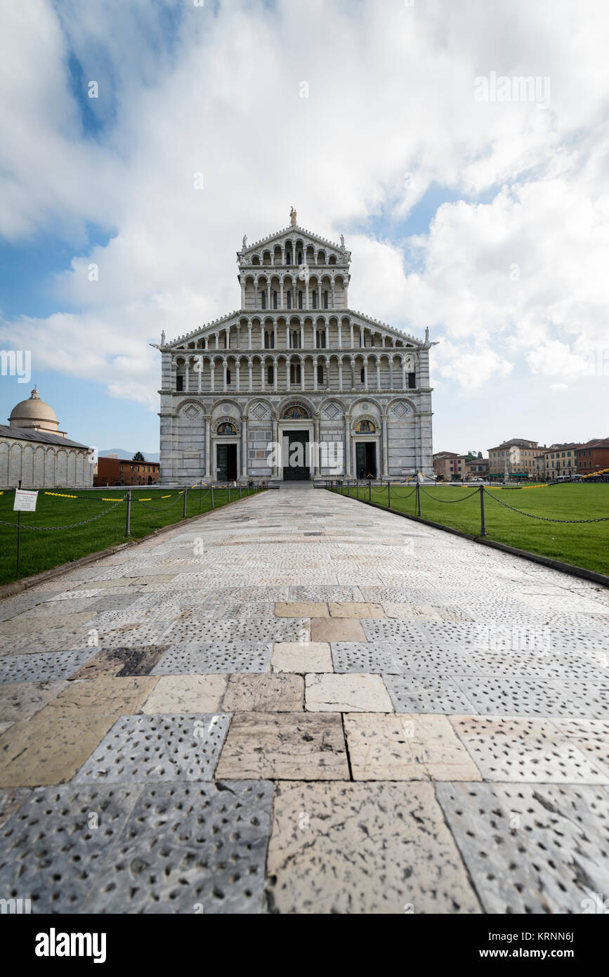 Color photograph of a tiled path leading to the Cathedral of Pisa (Italy), which is outlined against a background of blue sky with white clouds. Stock Photo