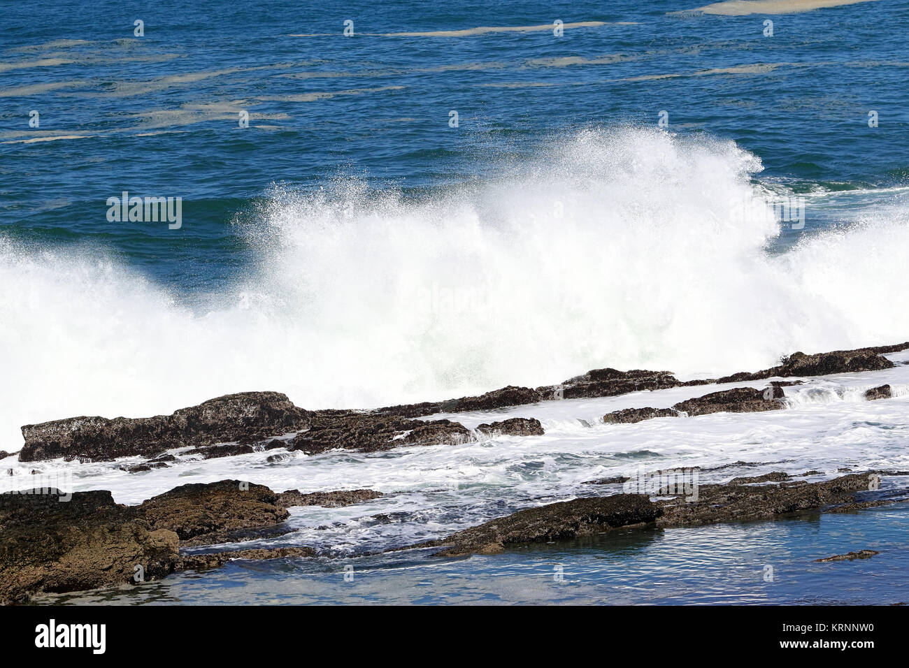 A big wave crashing into the rocks in the rough wild water of the ocean on a stormy during wintertime in South Africa. Stock Photo