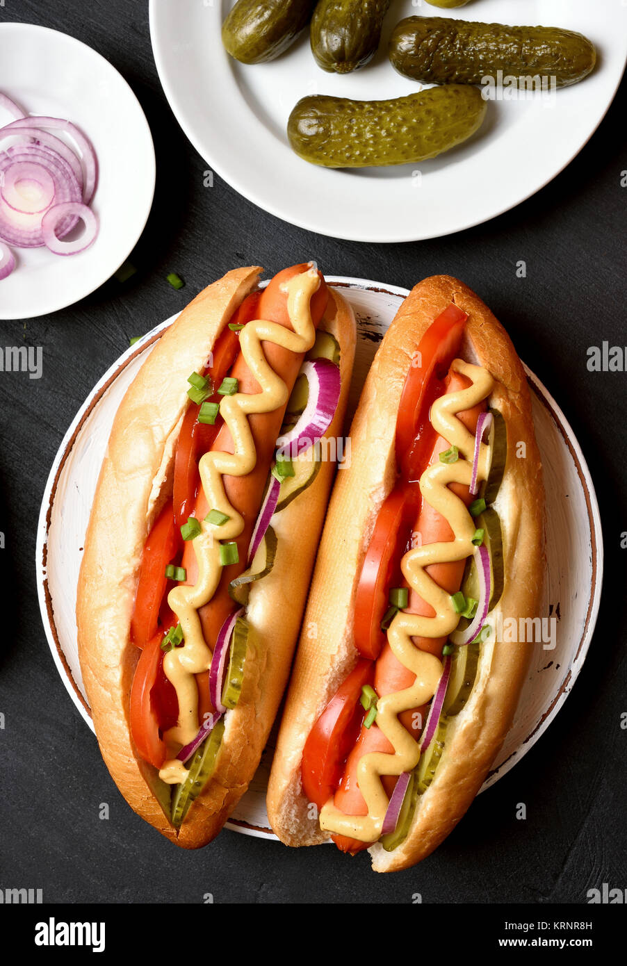 Tasty hot dogs with tomato, marinated cucumbers, onion on dark
