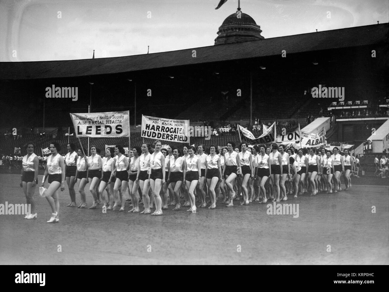 Demonstration by The Women's League of Health and Beauty, during the 1930s. Shows banners relating to  the Leeds, Harrogate, Huddersfield, and Dunstable branches. Demonstration inside a sports stadium, possibly Wembley. Stock Photo