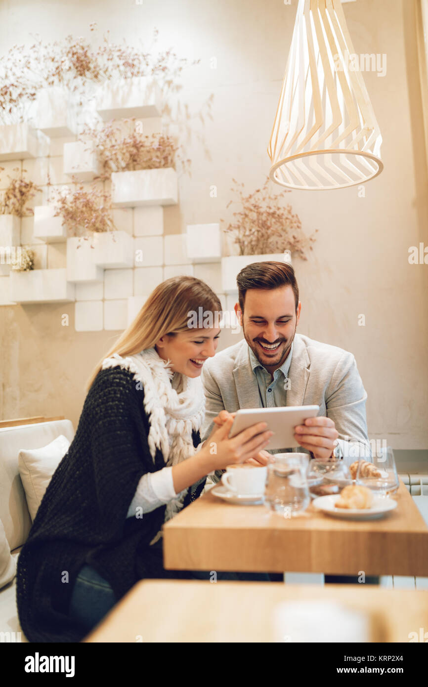 Two young smiling businesspeople talking and surfing the internet on digital tablet on a coffee break at cafe. Stock Photo