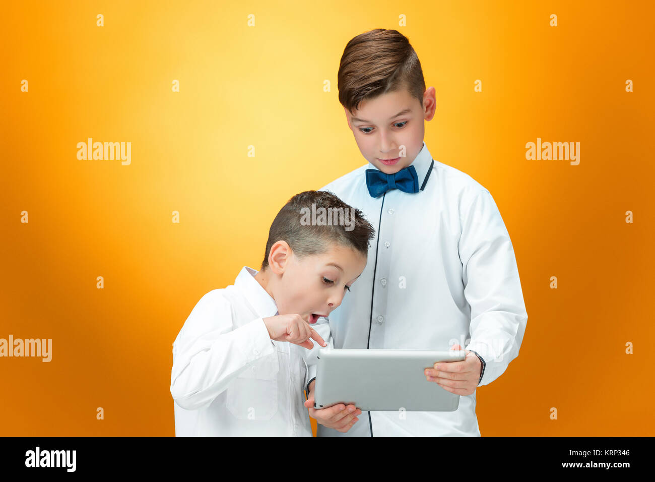 The two boys using laptop on orange background Stock Photo - Alamy