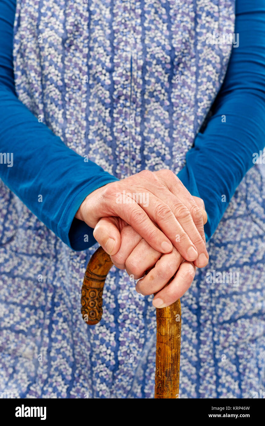 alte frau mit blauer schürze und stock hände übereinander Stock Photo