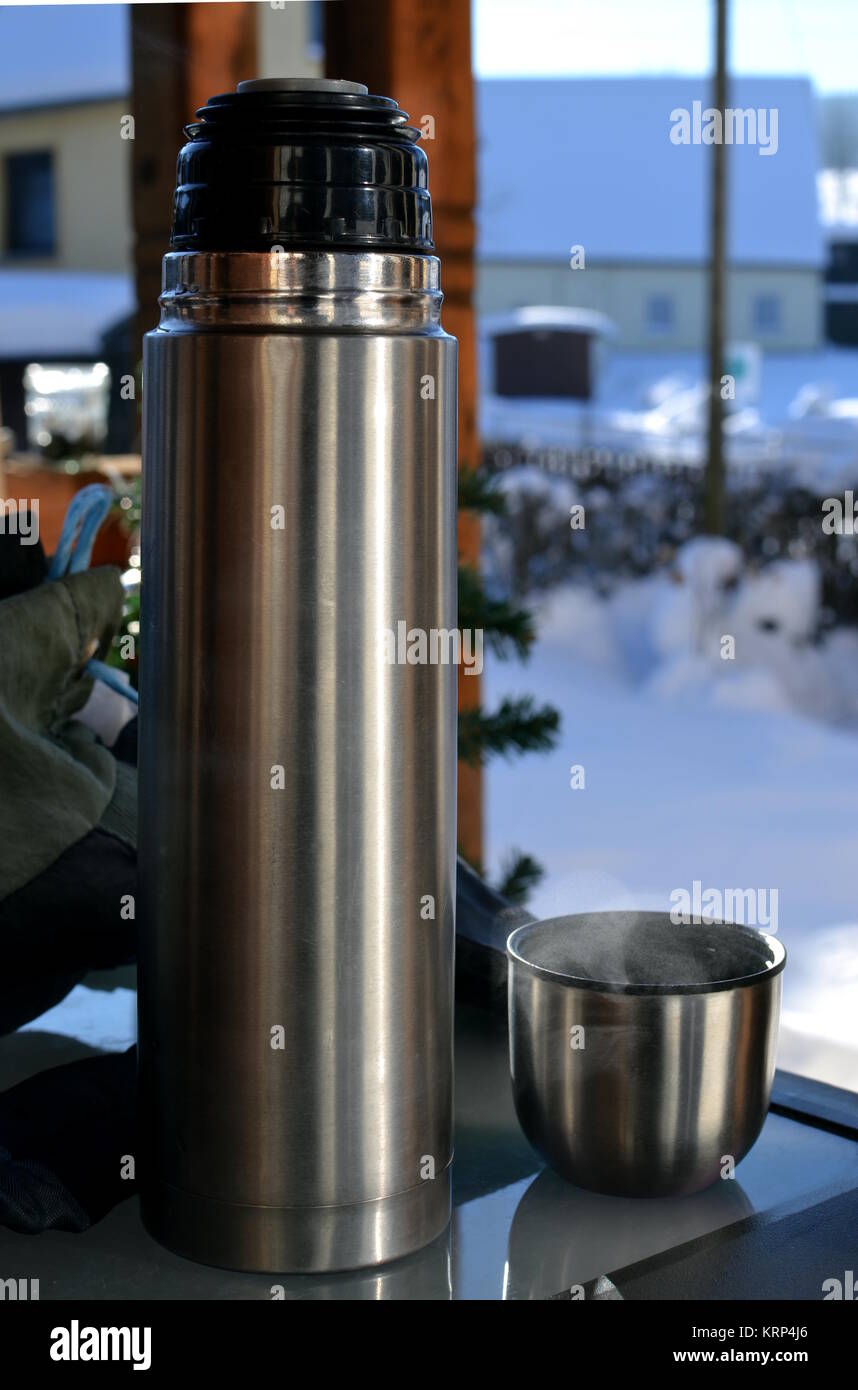 A thermos bottle and a cup of tea on a glass table and a snowy scene in the  background Stock Photo - Alamy