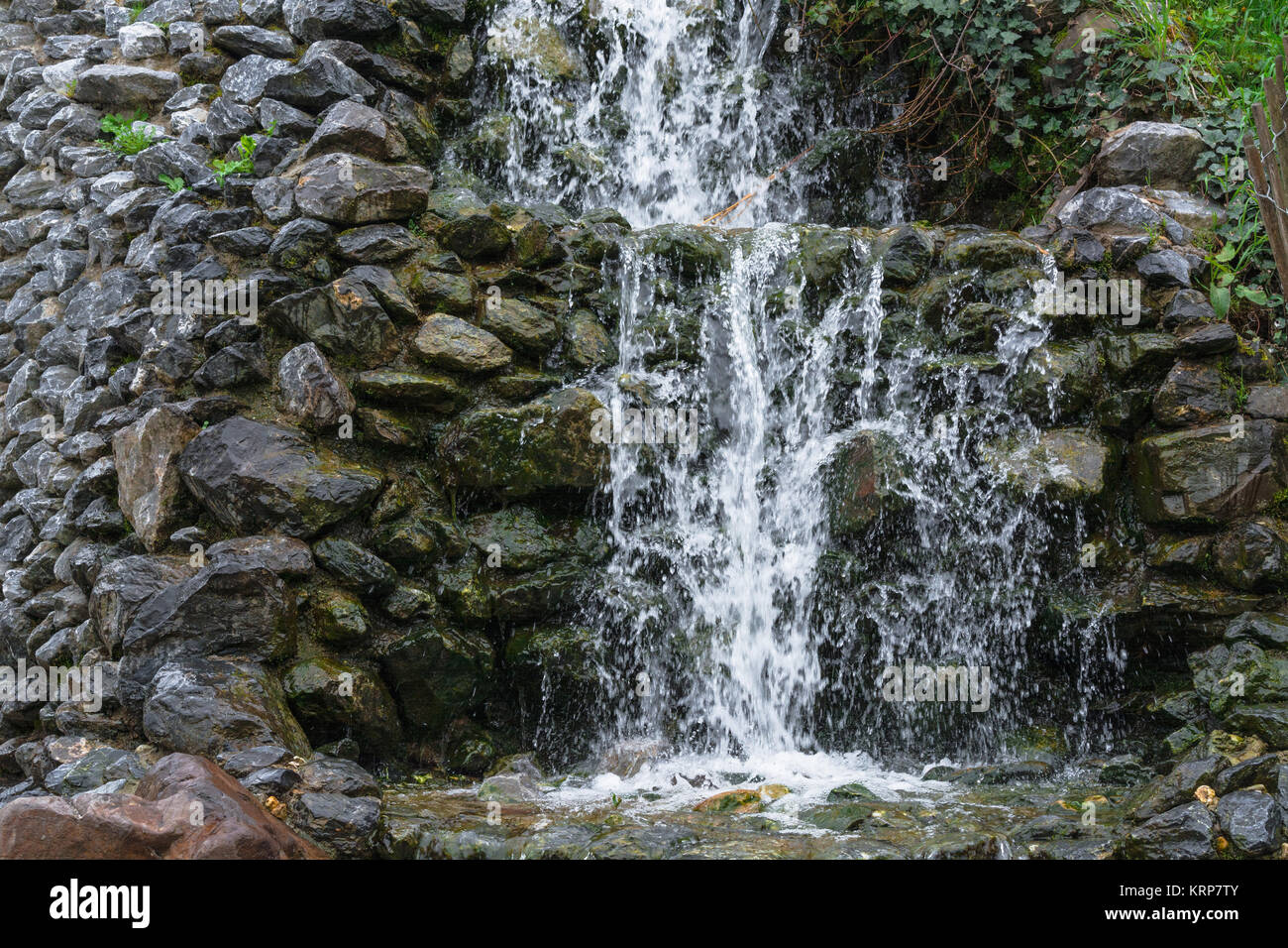 Kleiner Wasserfall, Kaskaden fließt über moosige Felsesteine in einem botanischen Garten. Stock Photo