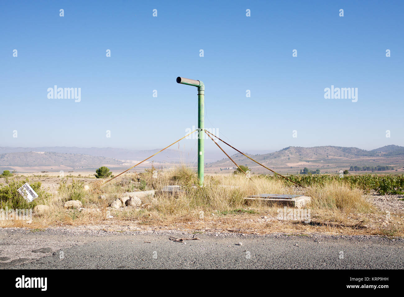 Single green pipe with 90 degree bend coming out of the ground in
