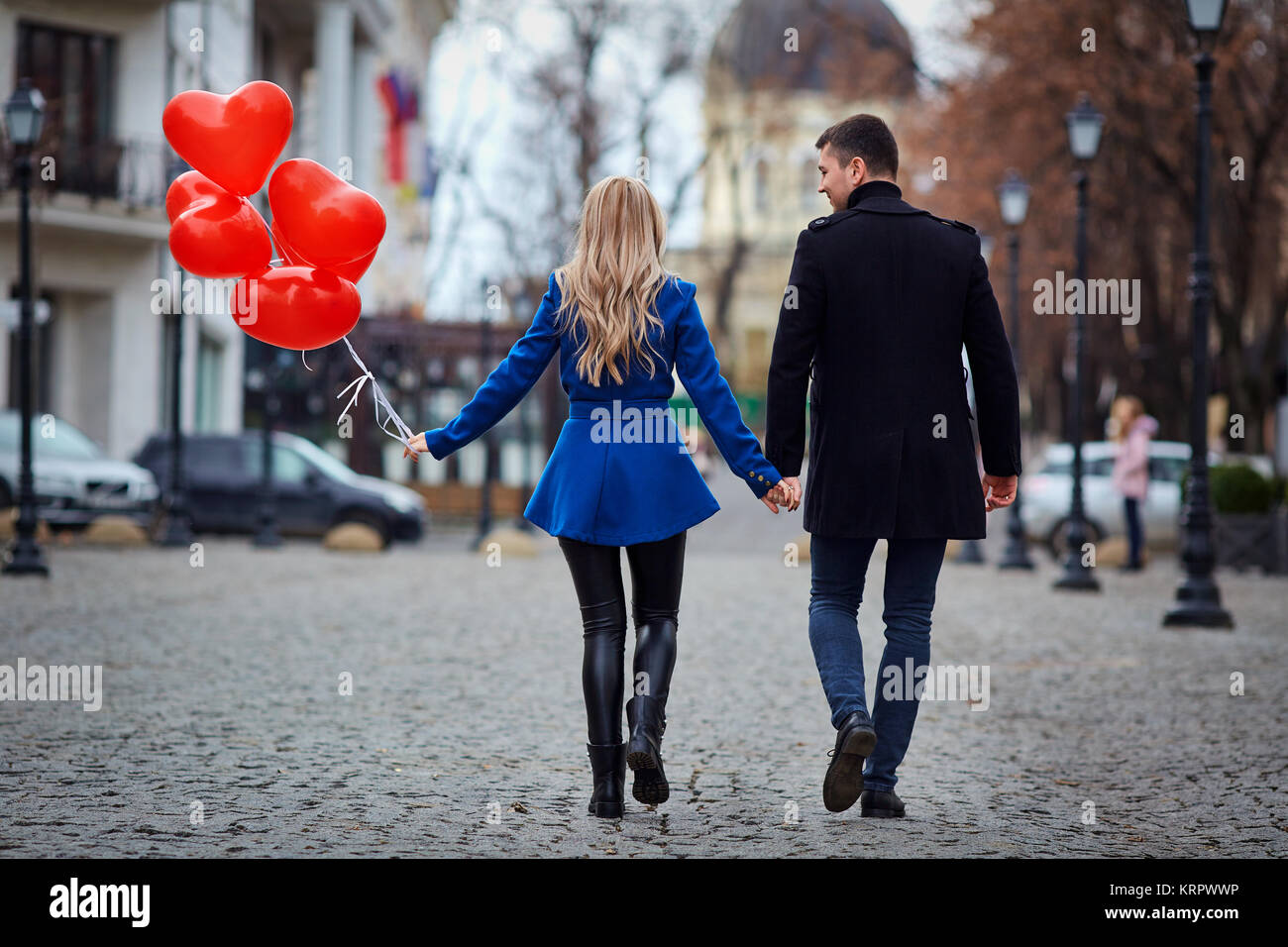 A young couple in a coat are holding a balloons heart in the cit Stock ...