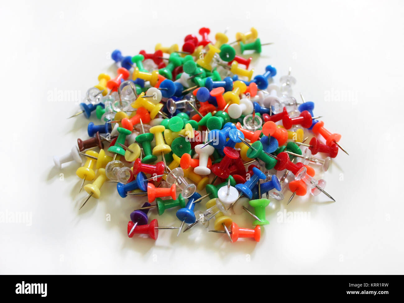 A pile of colorful thumb tacks on a white surface Stock Photo