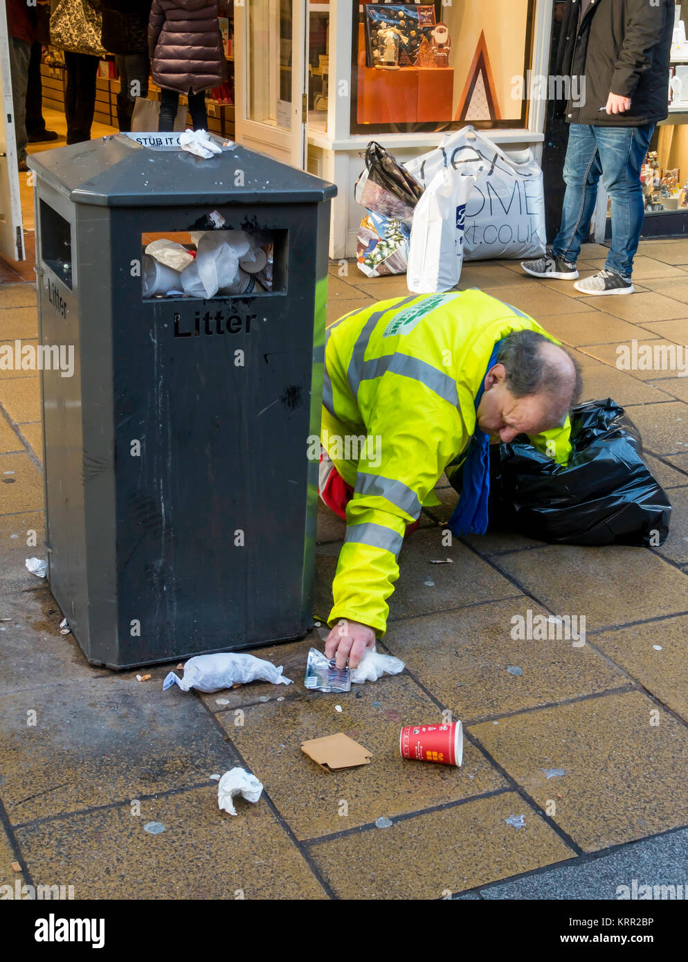 A Council worker on his hands and knees clearing up rubbish from an over filled litter bin in Darlington Town Centre Stock Photo