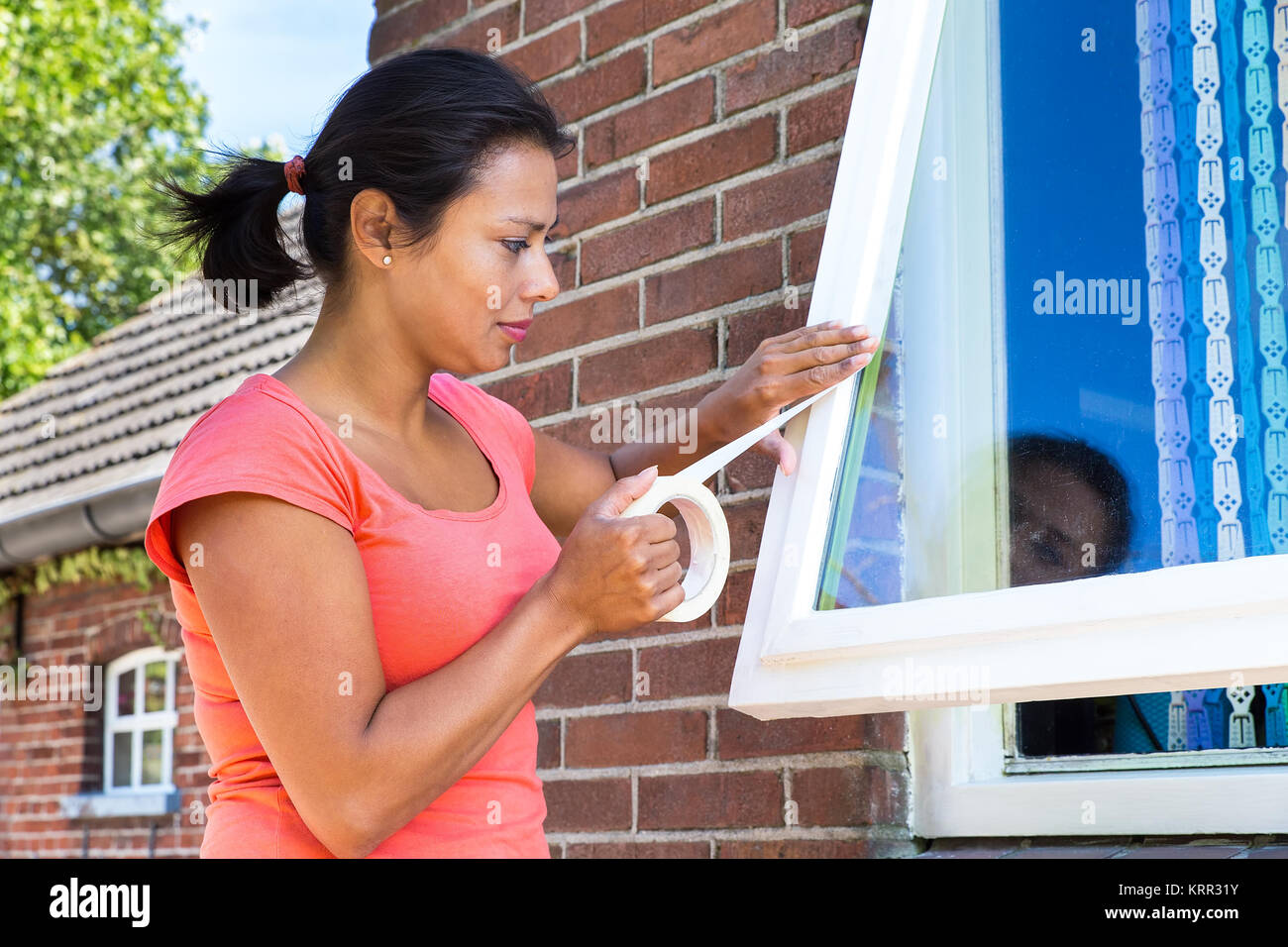 Young woman sticking adhesive tape on window glass Stock Photo