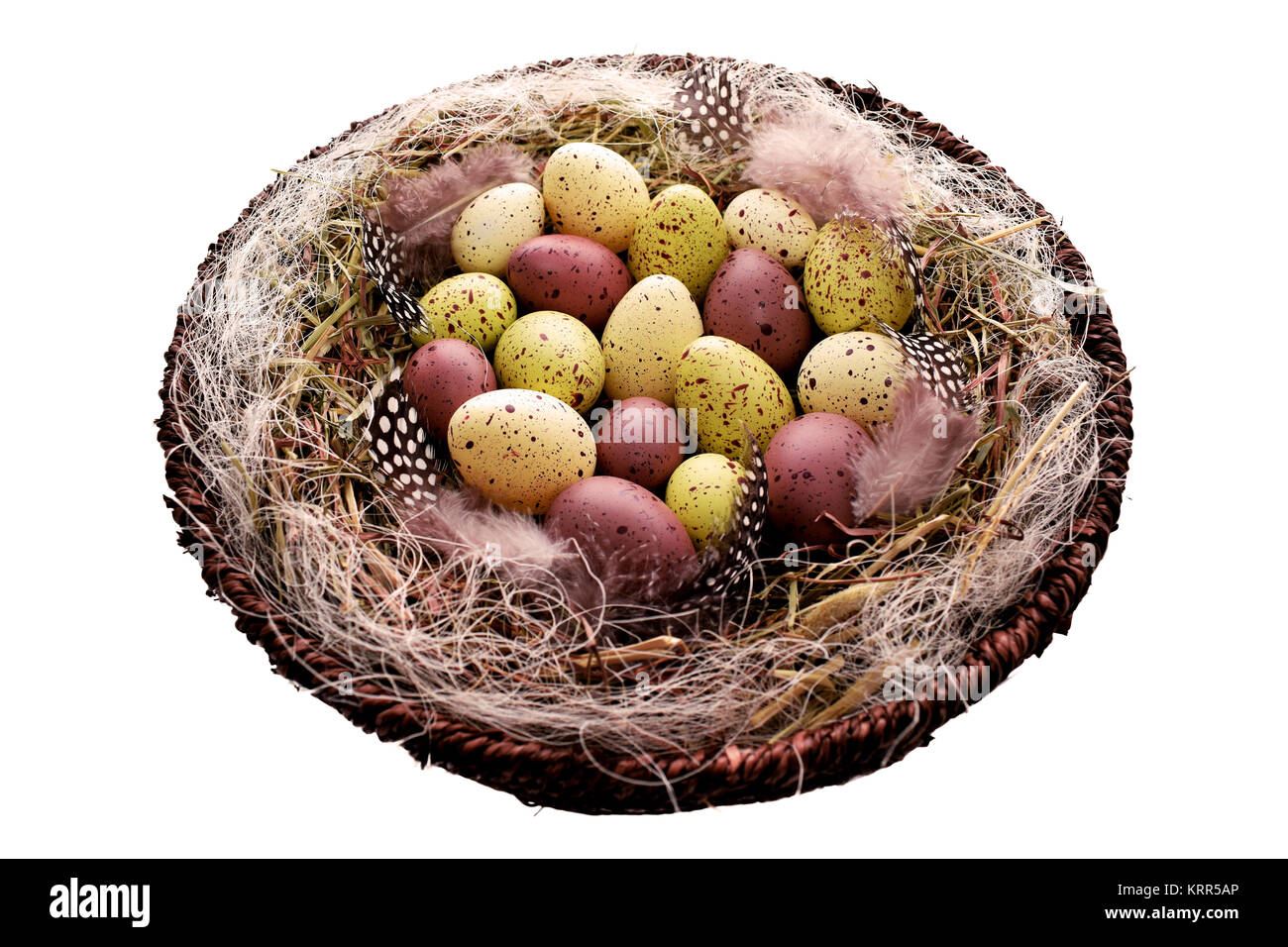 Decorative Easter eggs in basket with hay and Guinea fowl feathers Stock Photo