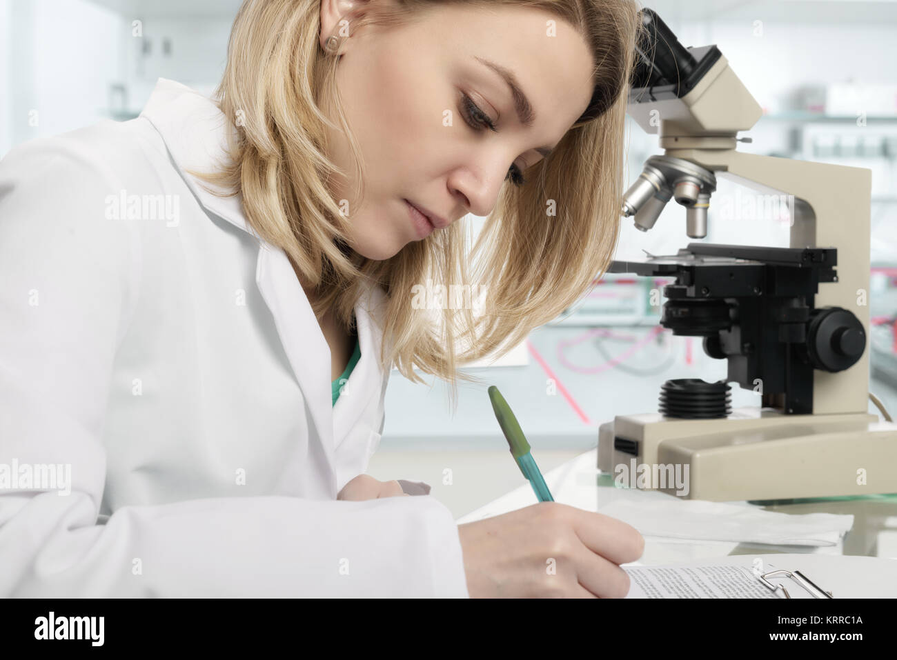 Young female scientist or tech writes report in modern laboratory, This image is toned. Stock Photo