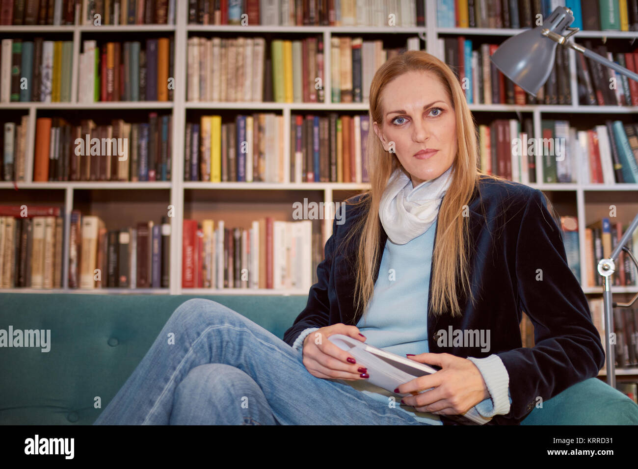 one woman, posing, looking at camera, holding magazine. shelf full of books behind (out of focus). Stock Photo