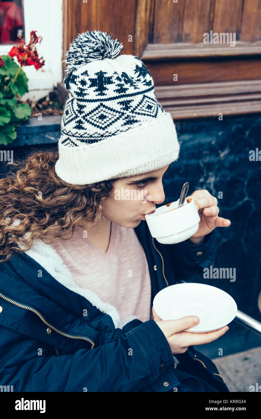 A teenage girl is sitting in a terrace and is drinking a cup of  Stock Photo