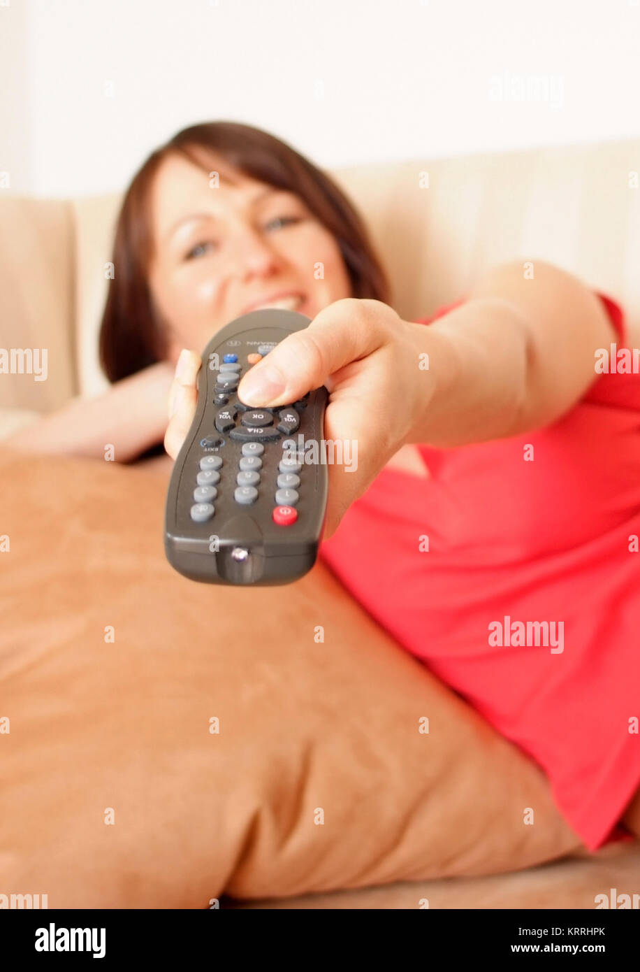 Junge Frau liegt mit Fernbedienung auf Couch - young woman with remote control on couch Stock Photo