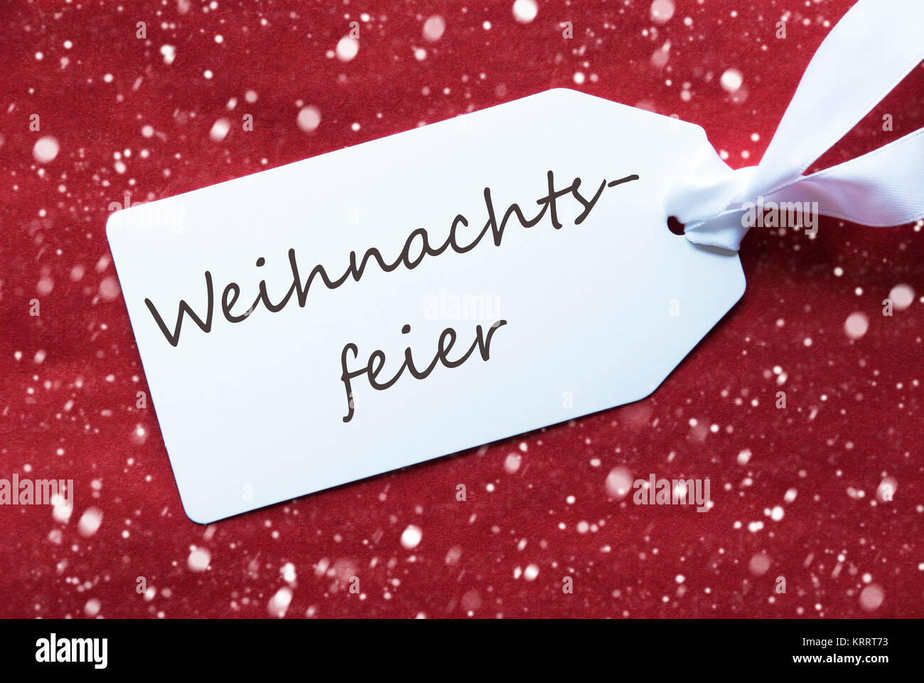 German Text Weihnachtsfeier Means Christmas Party. One White Label On A Red Textured Background. Tag With Ribbon And Snowflakes. Stock Photo